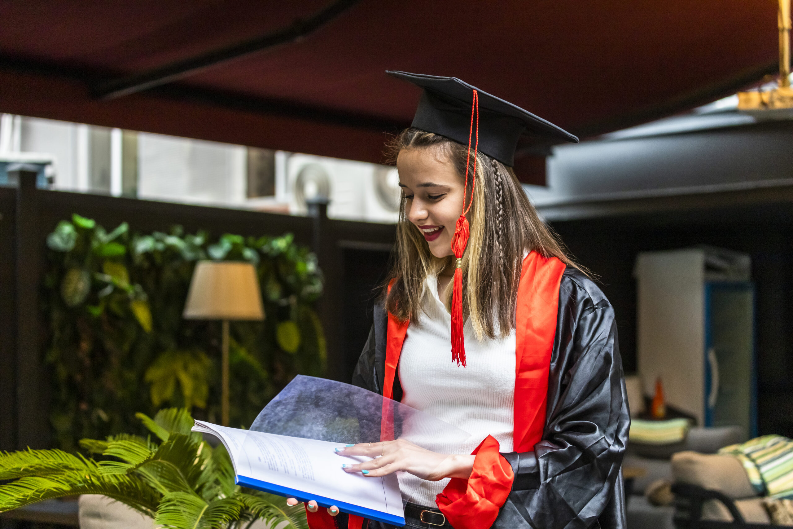 Young student wearing graduation cape and looking at to her notebook. High quality photo